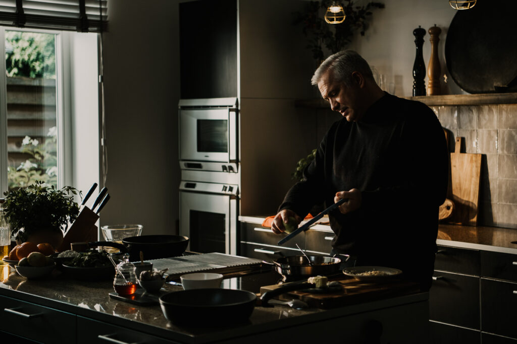 Alexander Herrmann reibt Zutaten in einen Topf während des Kochens, dynamischer Moment in moderner Küche, festgehalten von einem erfahrenen Werbefotograf-berlin.