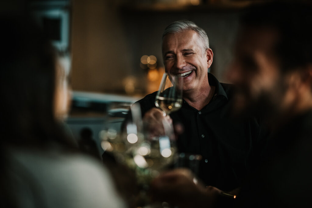 Alexander Herrmann lacht andere Gäste am Esstisch an – Werbefotografie von Werbefotograf Berlin