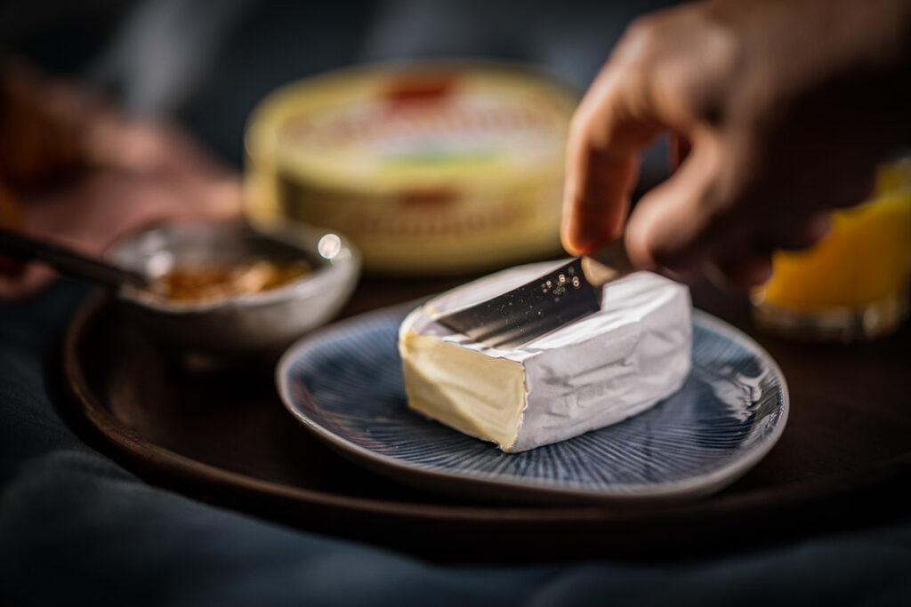 Französischer Weichkäse Géramont, mit Messer angeschnitten, auf Teller angerichtet, Foodfotografie.