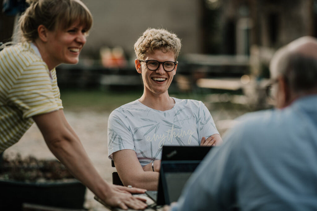 Team in Besprechung während einer Workcation in Brandenburg, entspannte Arbeitsatmosphäre im Grünen, festgehalten vom Businessfotograf, Teilneher lauchen sich an.
