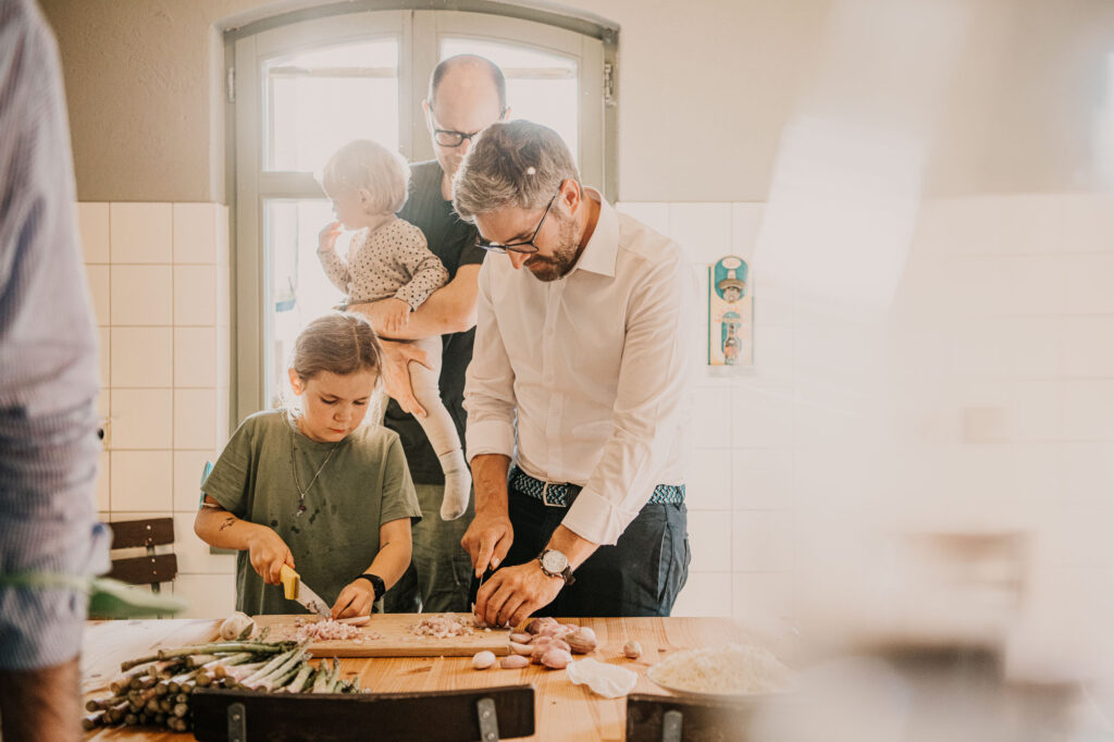 Teilnehmer eines Workcation-Business-Meetings schneiden gemeinsam Gemüse beim Kochen in entspannter Businesskleidung