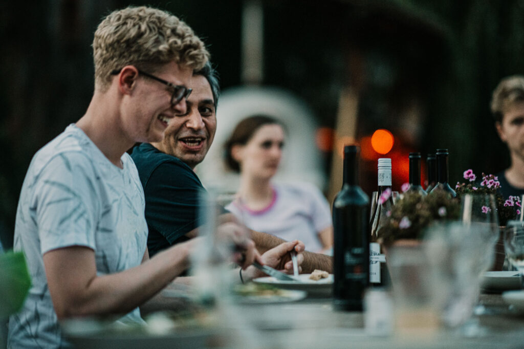 Mann lacht entspannt am Abendessentisch nach einem Business-Meeting – authentische Szene aus einer Businessreportage fotografiert bei einem Networking-Dinner gemeinsam mit anderen Teilnehmern