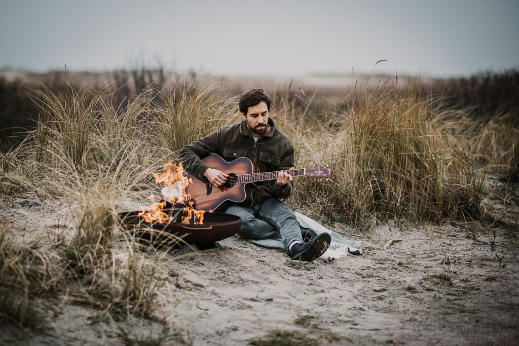 Businessportrait von Max Giesinger beim Gitarre Spielen am Feuer in Sankt Peter Ordnings Dünen am Strand fotografiert von professionellem Businessfotografen für DB Mobil magazin – professionelles Musiker- und Werbefoto.