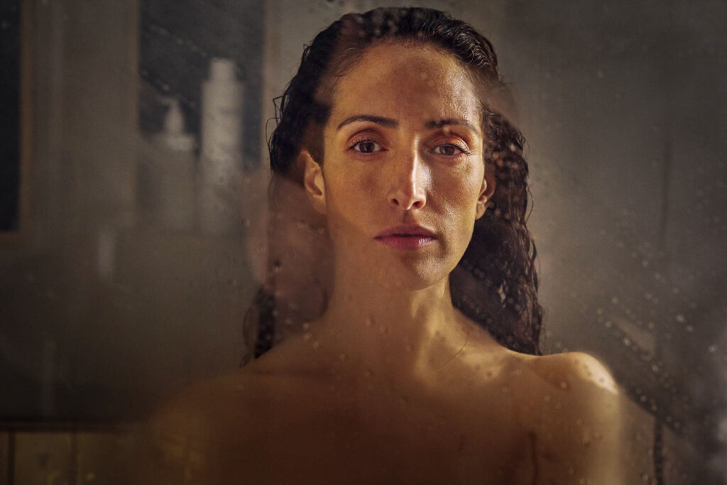 Dunkelhaarige Frau hat geduscht und schaut durch beschlagene Duschglasscheibe – starkes Portrait, Werbefotografie, Werbefotograf Berlin.