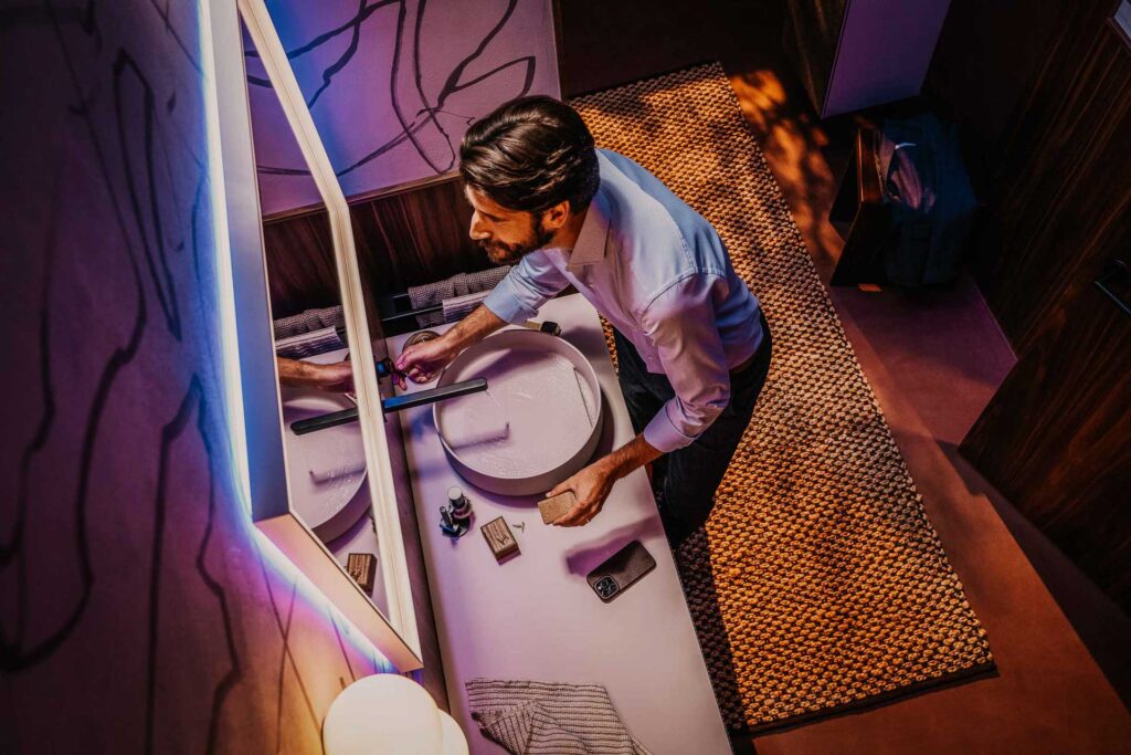 Mann lässt Wasser in Waschbecken laufen und schaut sich im Spiegel an, Nachtstimmung – Werbefotografie, Werbefotograf Berlin.