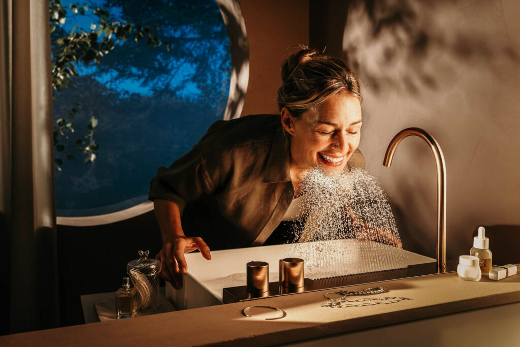 Frau duscht lachend ihr Gesicht unter neuartiger Wasserfall-Regensäule von Hansgrohe – Keyvisual Werbefotografie, Werbefotograf Berlin.