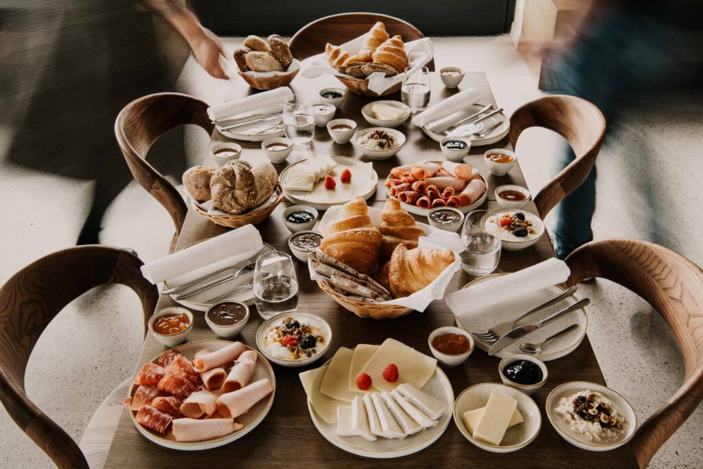 Vollständig eingedeckter Frühstückstisch im Restaurant, während unscharf vorbeilaufende Kellner für lebendige Atmosphäre sorgen – hochwertiges Visual für professionelle Hospitality-Fotografie.