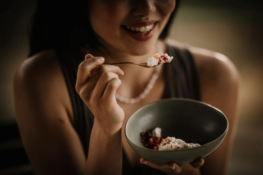 Asiatische Frau hält eine Gabel mit Käse-Vorspeise kurz vor dem Mund – Genussmoment im moody Licht, hochwertiges Werbefoto für Fissler von Werbefotograf Berlin