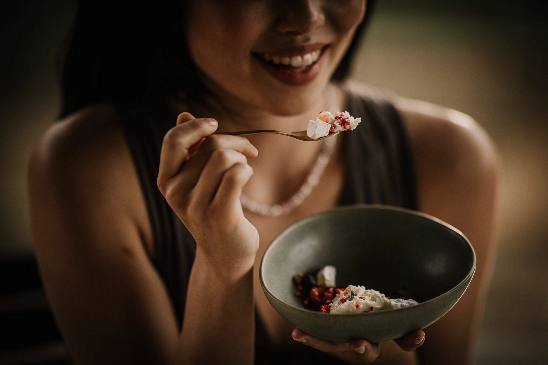Atmosphärischer Moment voller Genuss und Eleganz. Asiatische Frau hält eine Gabel mit Käse-Vorspeise kurz vor dem Mund – Genussmoment im moody Licht, hochwertiges Werbefoto für Fissler von Werbefotograf Berlin