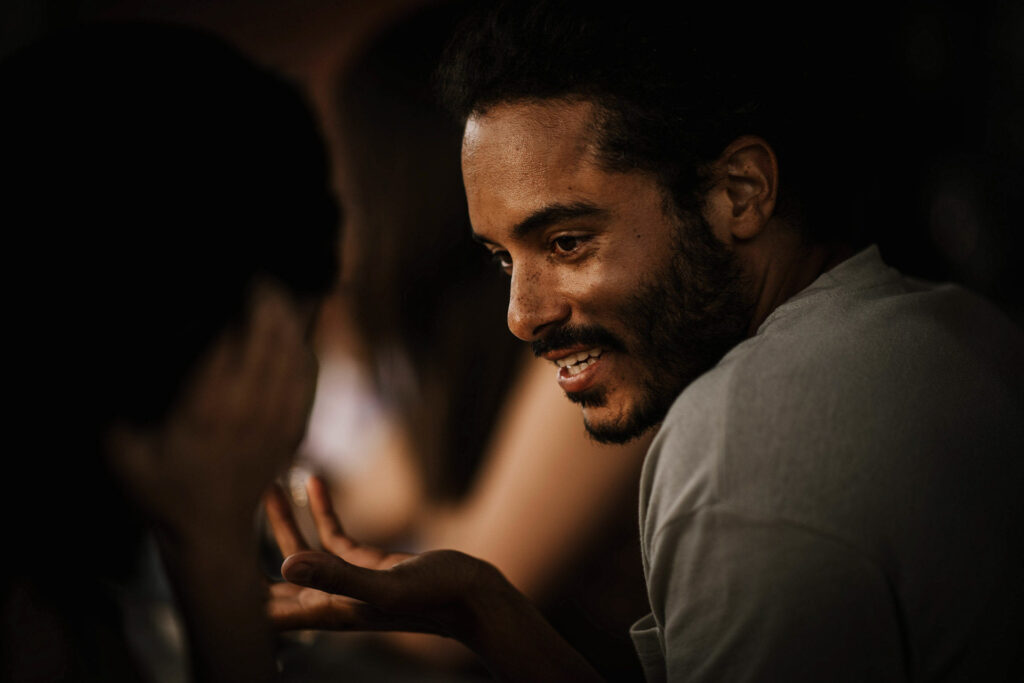 Mann mit Sommersprossen und Afro-Locken unterhält sich am Esstisch mit einer Person, während ein warmer Vorspeisenteller davor steht – stimmungsvolles Werbemotiv für Fissler von Werbefotograf Berlin Malte Jäger