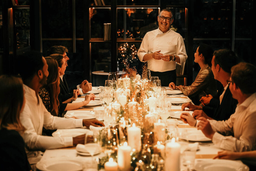 Headchef erklärt lachend das Menü an einer langen, festlich gedeckten Kerzentafel im Sofitel während der Festive Season – Hotelfoto für Hospitality-Marketing