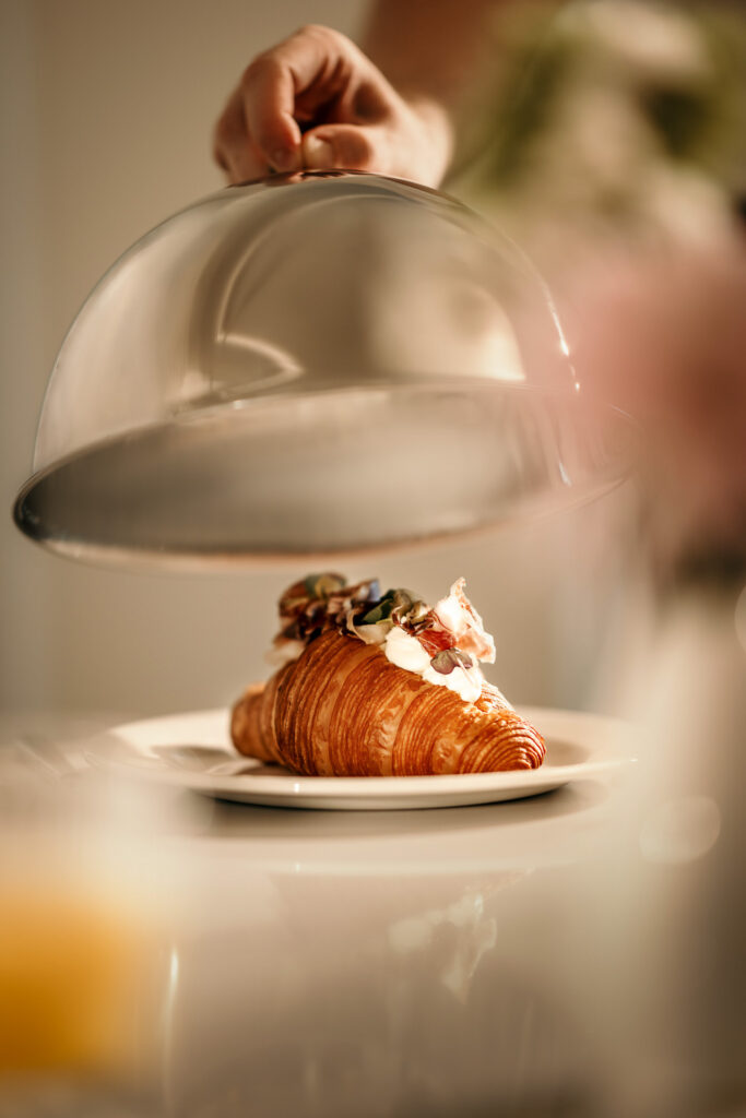 Frisch belegtes, hochwertiges Croissant unter einer Gloche auf elegantem Teller – Werbefotograf für Hospitality-Marketing
