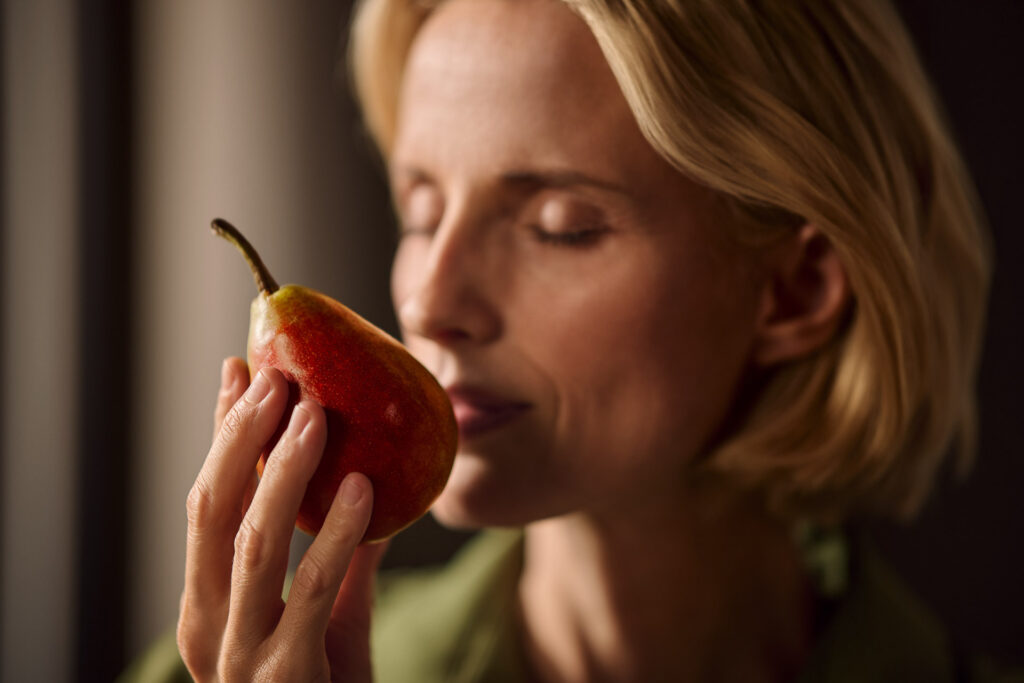 Schöne Frau riecht genüsslich an einer Birne, kurz vor dem Essen – aufgenommen vom Werbefotograf Berlin.