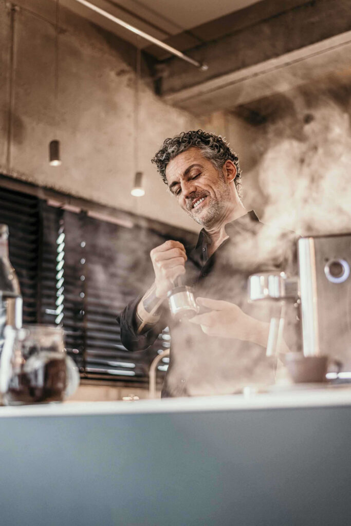 Mann bedient Espressomaschine in privater Küche, es dampft und zischt – Werbefotos für WMF mit Agentur Ogilvy, stimmungsvolle Produktfotografie.