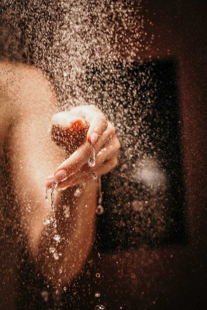 Werbefotografie Nahaufnahme der Hand einer Frau, aus der Wasser aus einem Hansgrohe-Duschstrahl tropft – ästhetisches Werbefoto in rotem Design-Badezimmer.