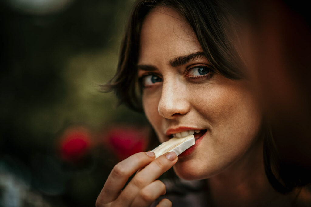 „Close-up einer französischen Frau, die in ein Stück Geramont-Käse beißt – authentisches Werbefoto für Lifestyle- und Food-Marketing.“