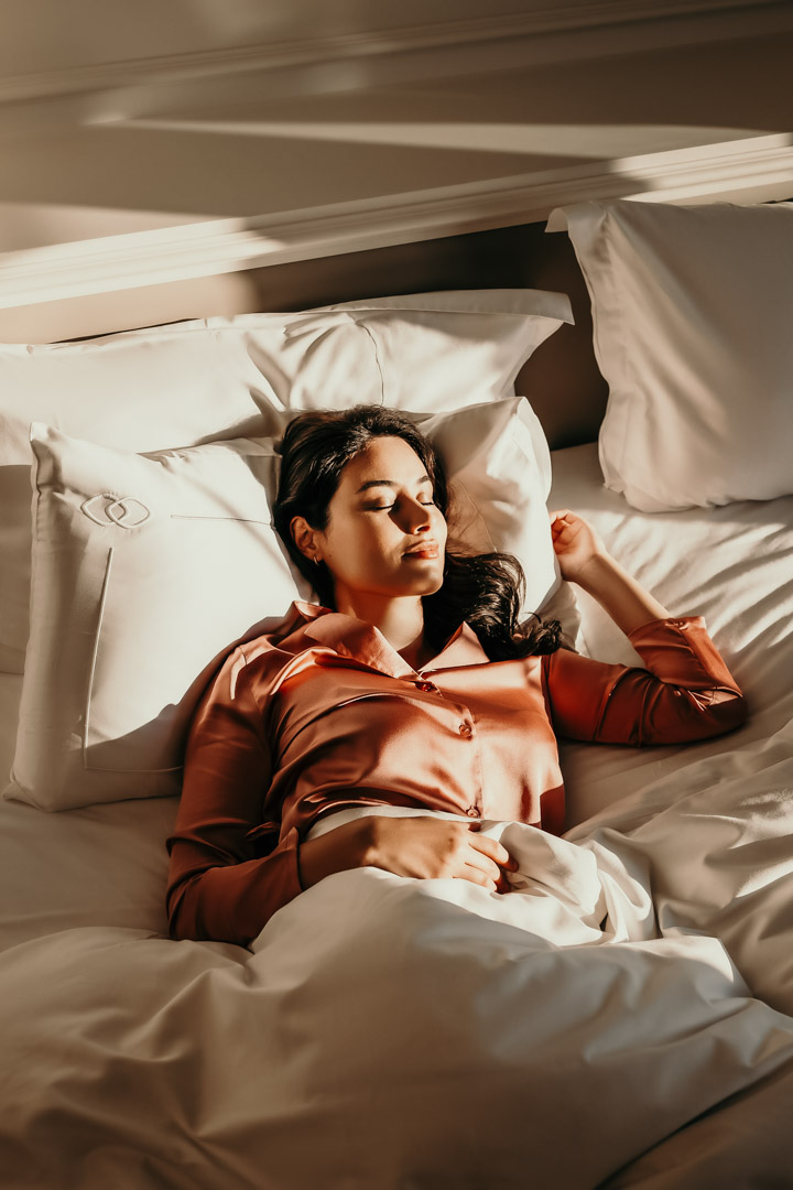 Werbefotografin Magdeburg: Hospitality-Aufnahme im Premium-Hotel Magdeburg – Frau in rosa Schlafanzug liegt entspannt im Bett, hochwertige weiße Bettwäsche, elegante Lifestyle-Stimmung, perfekt für Werbefotografie, Hotel-Marketing und Social Media.
