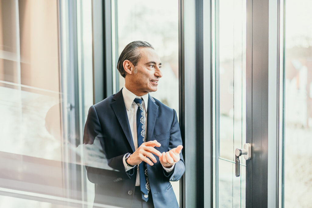 CEO Vito Volpe von der Santander Bank steht am Fenster, spricht und lächelt professionell – Businessportrait von Businessfotograf Berlin“